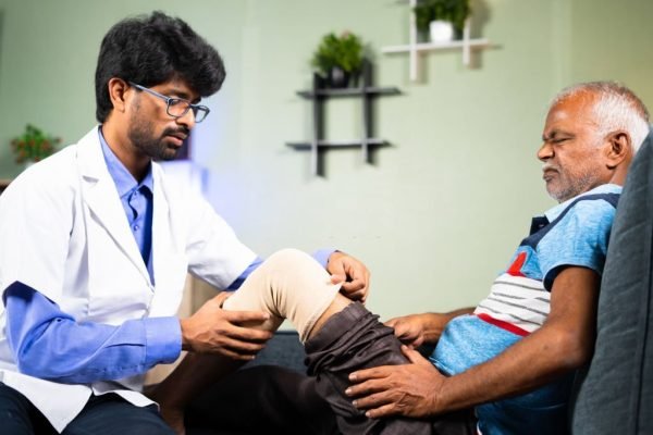 Orthopedic Physician treating or helping old man to wear knee support braces at home - concept of arthritis, sprain treatment and Doctor consultation at Home